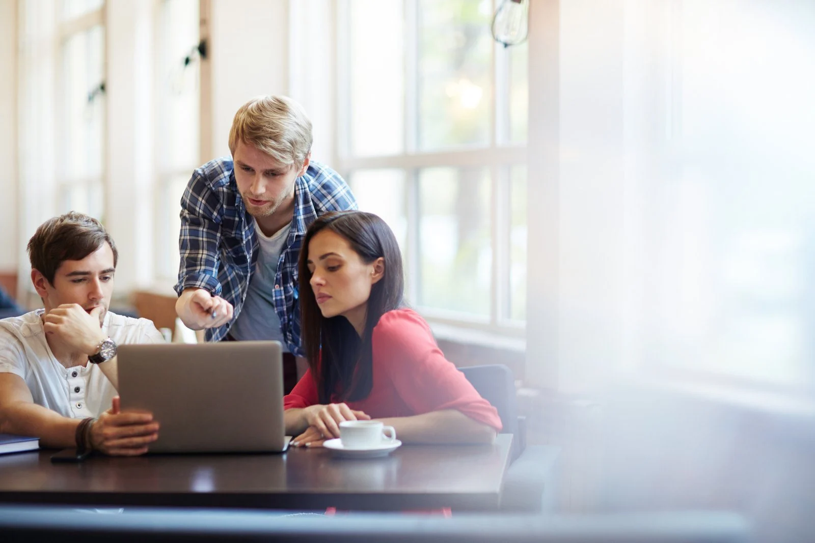 A tutor helping two students at a laptop